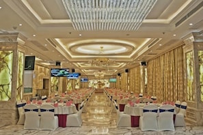 Un salón de banquetes con filas de mesas, candelabros y amplias ventanas.