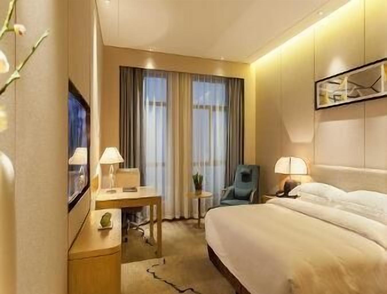 Una habitación de hotel con una cama, un escritorio, una silla y una ventana con cortinas.