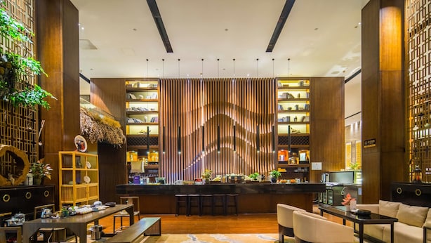 A modern bar area with a central bar counter, seating arrangements, and a decorative wall with vertical slats. - Ramada Plaza by Wyndham Changsha South (Changsha)