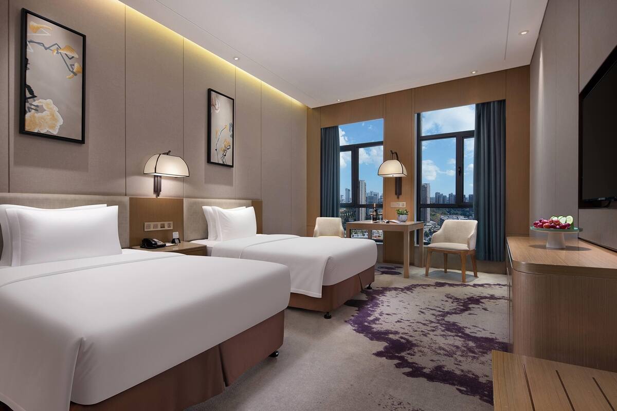 Une chambre d’hôtel avec deux lits, un bureau, une chaise, une télévision et une vue sur la ville.