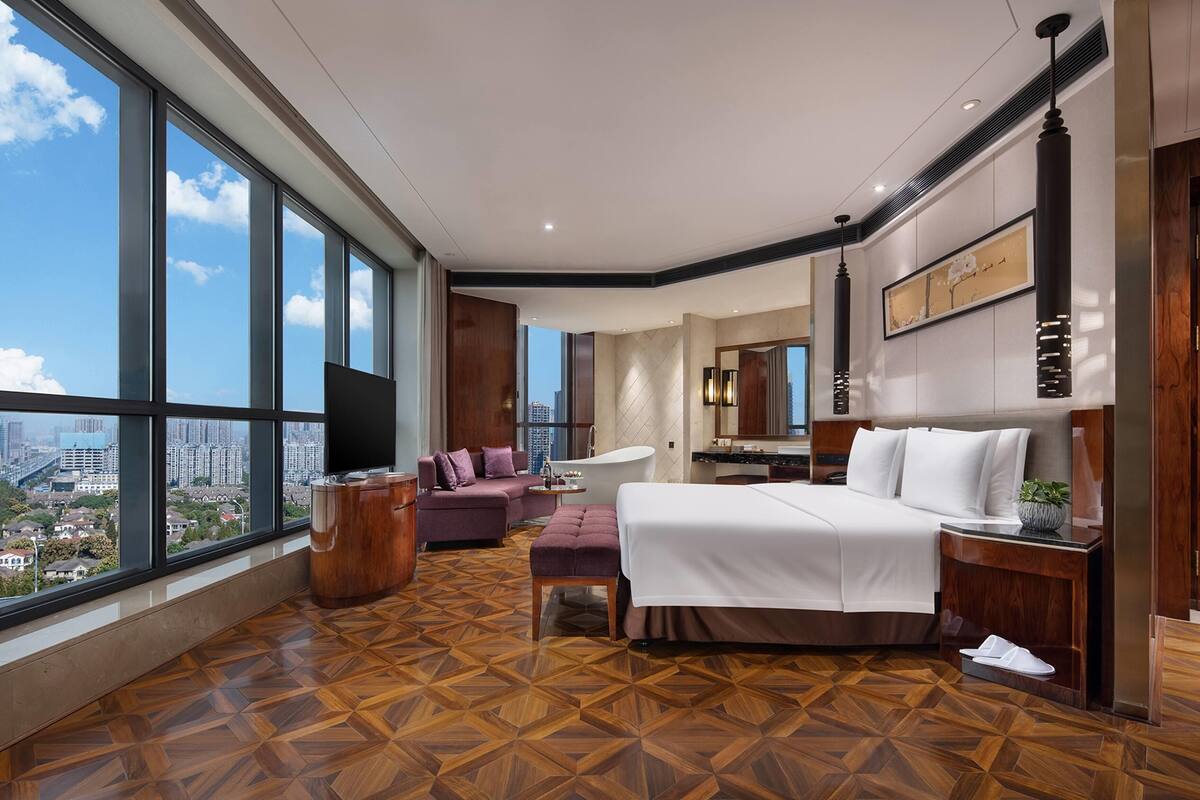 Une chambre d’hôtel moderne dotée d’un grand lit, d’un canapé, d’une coiffeuse et offrant une vue sur la ville.