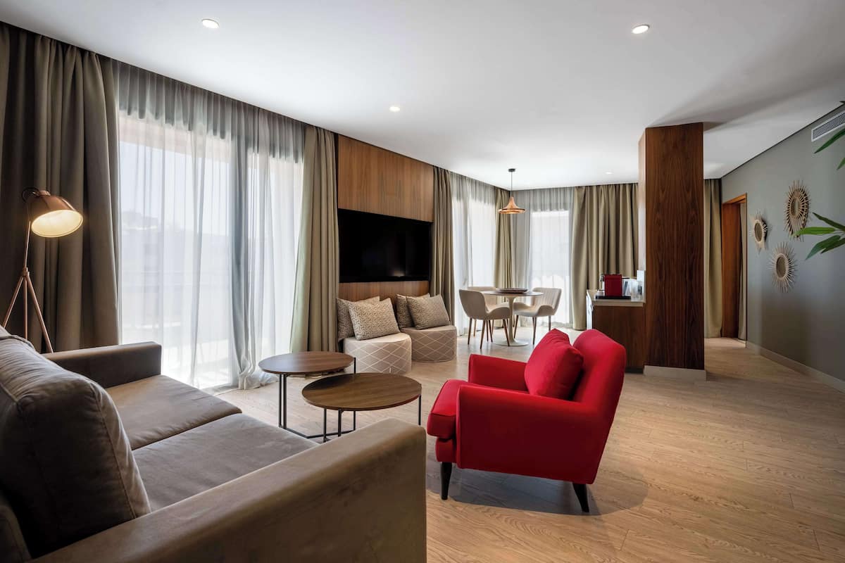 Un salon moderne avec un canapé, un fauteuil rouge et un téléviseur fixé au mur.