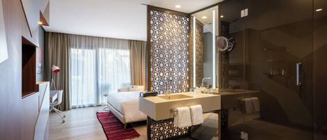 A modern hotel room with a large bed, a separate bathroom with a glass shower, and a desk with a chair.