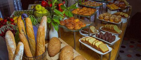 Una mesa de buffet con panes, pasteles y frutas variadas.