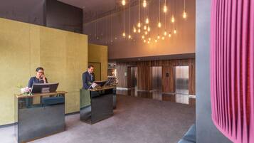 A modern reception area with two receptionists at desks, a large chandelier, and a wood-paneled elevator.