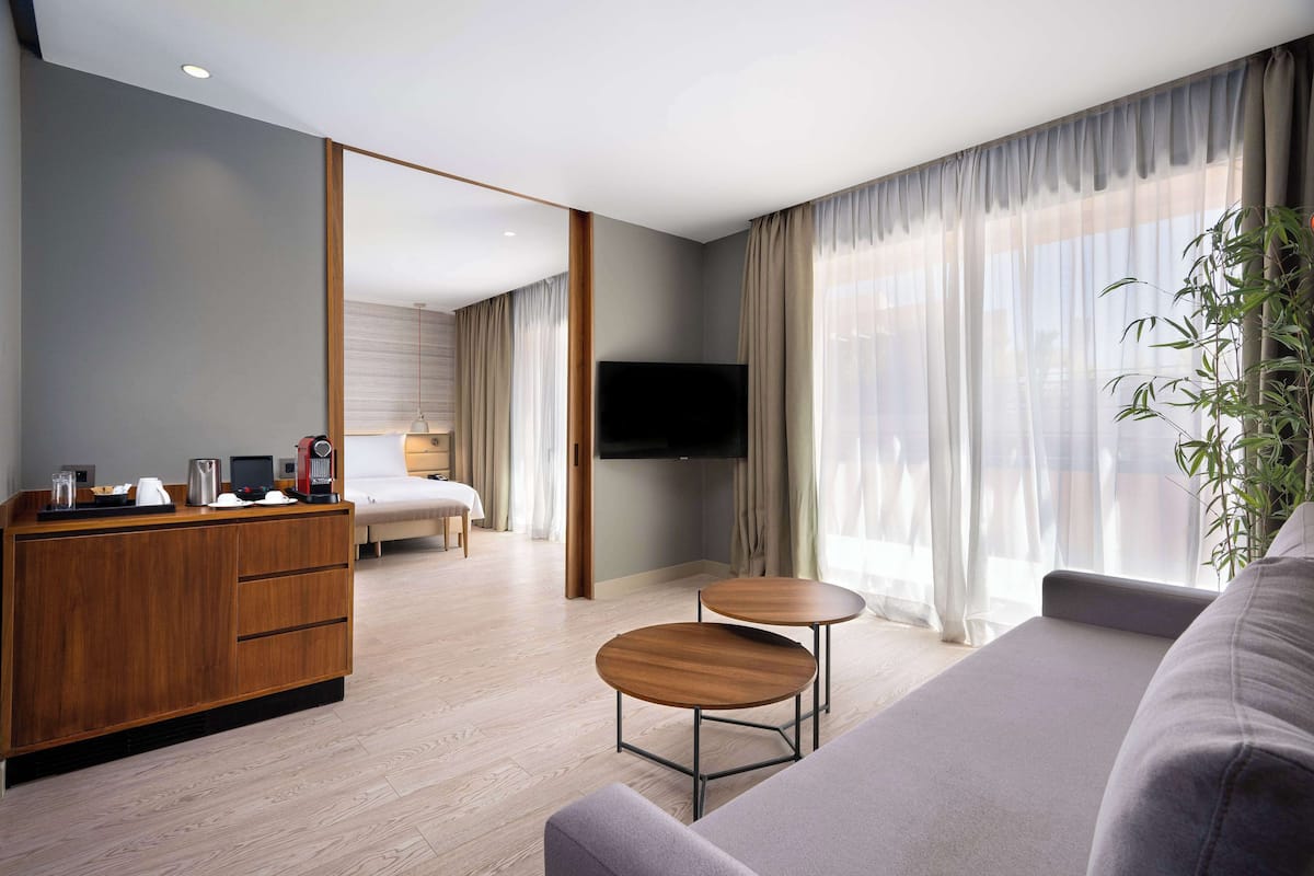 Une chambre d’hôtel moderne avec un bureau en bois, deux petites tables rondes, un canapé, un lit et un téléviseur.