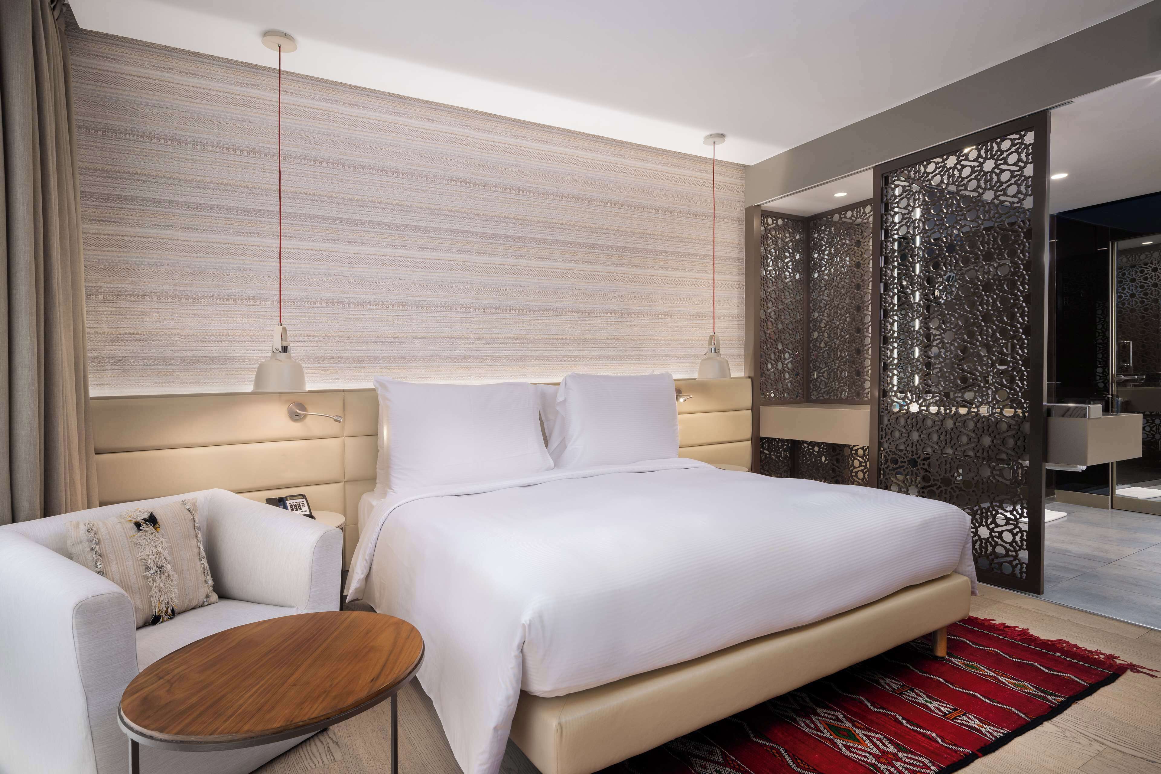 A modern hotel room with a large bed, a sofa, a small table, and a decorative wall panel.