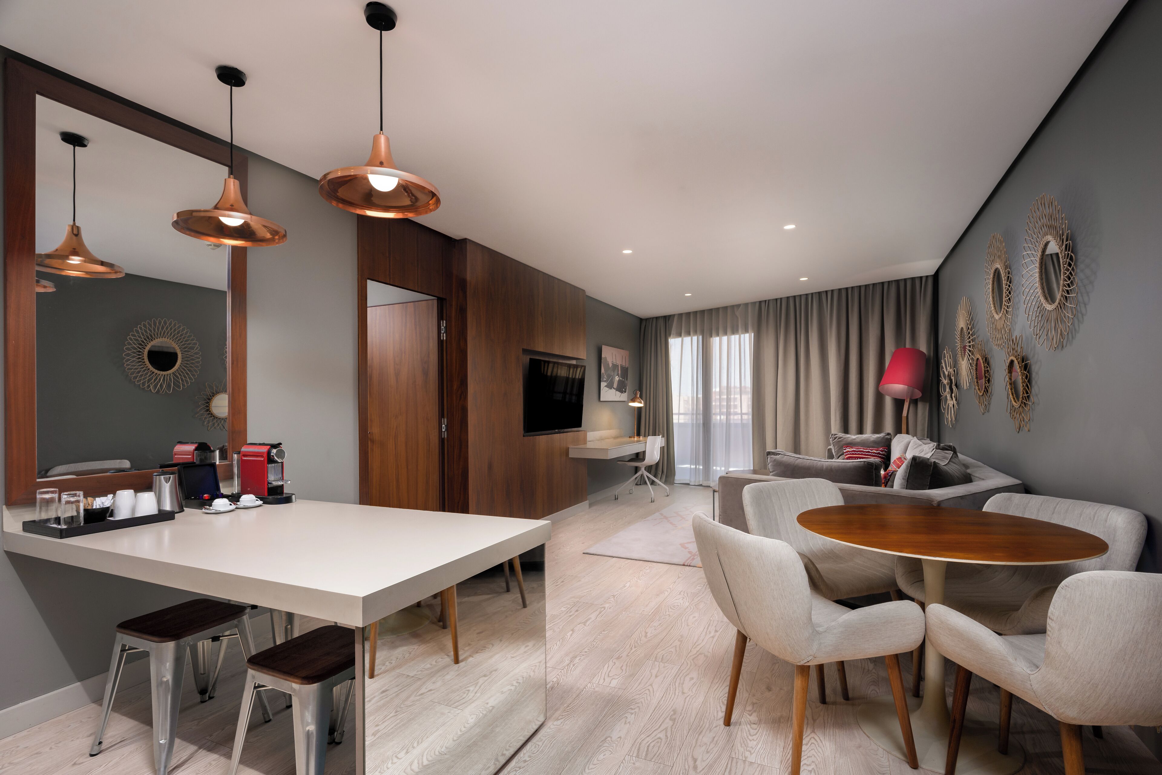 A modern living room with a dining area, a kitchen with a coffee machine, and a TV.