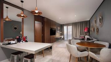 Una sala moderna con comedor, una cocina que incluye una cafetera y un televisor.