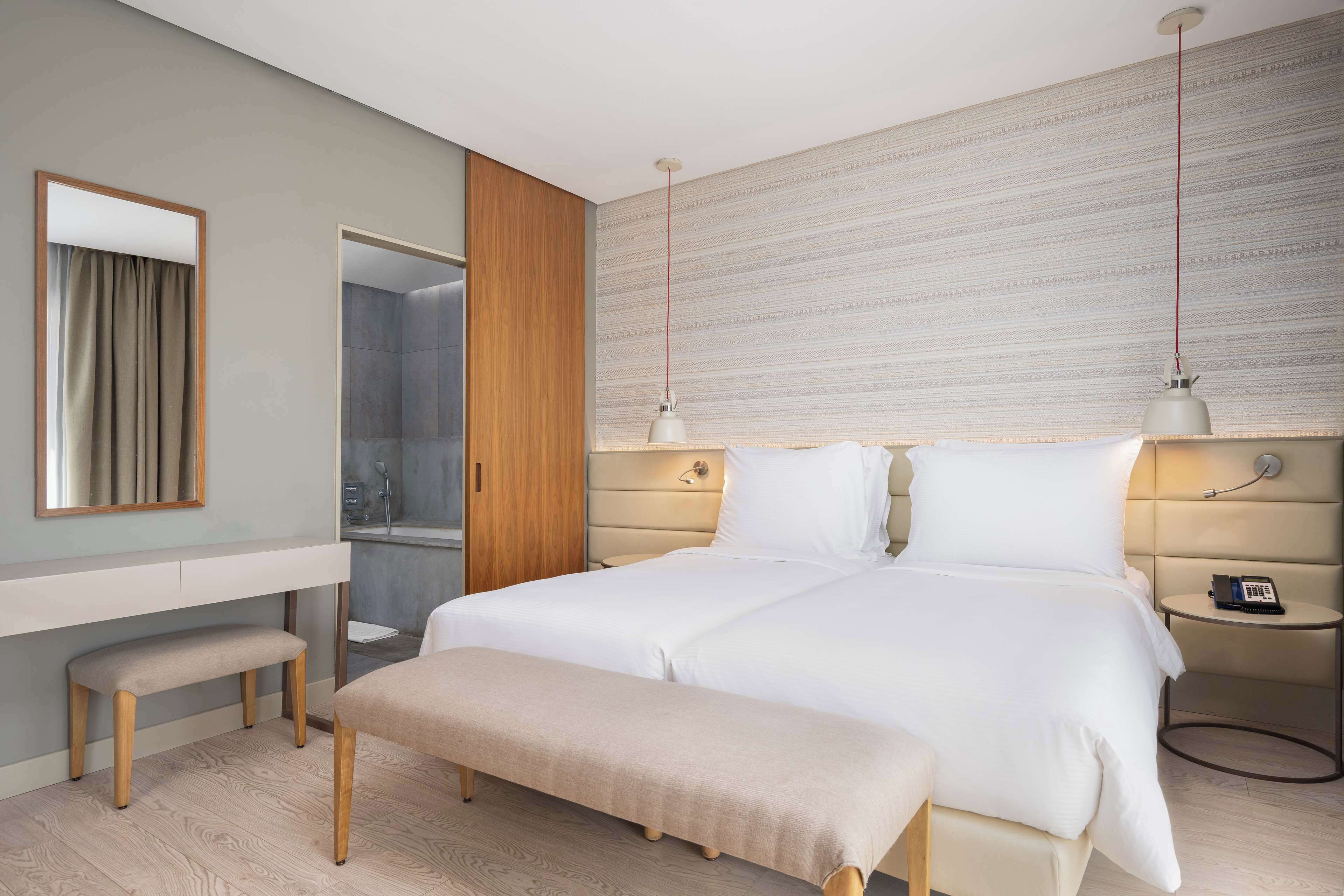 Et moderne hotelværelse med en stor seng, sengeborde, en bænk, et spejl og et bruseområde.