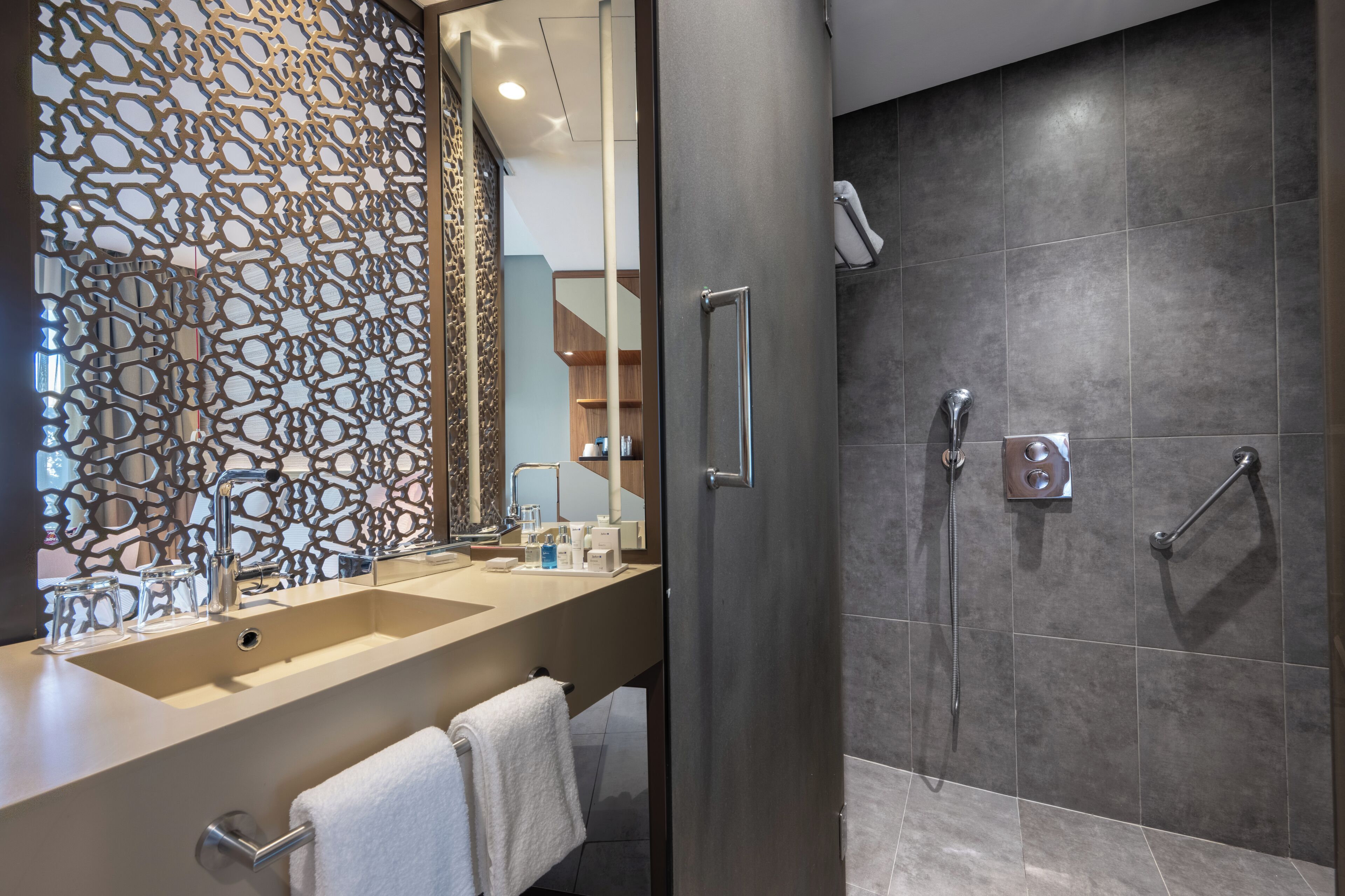 Un baño moderno con un espejo grande, dos lavamanos, ducha con cabezal de ducha manual y un panel decorativo en la pared.