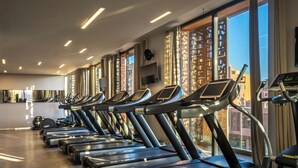 A row of treadmills in a gym with large windows and a modern ceiling design. - Radisson Blu Hotel, Marrakech Carré Eden (Marrakech)