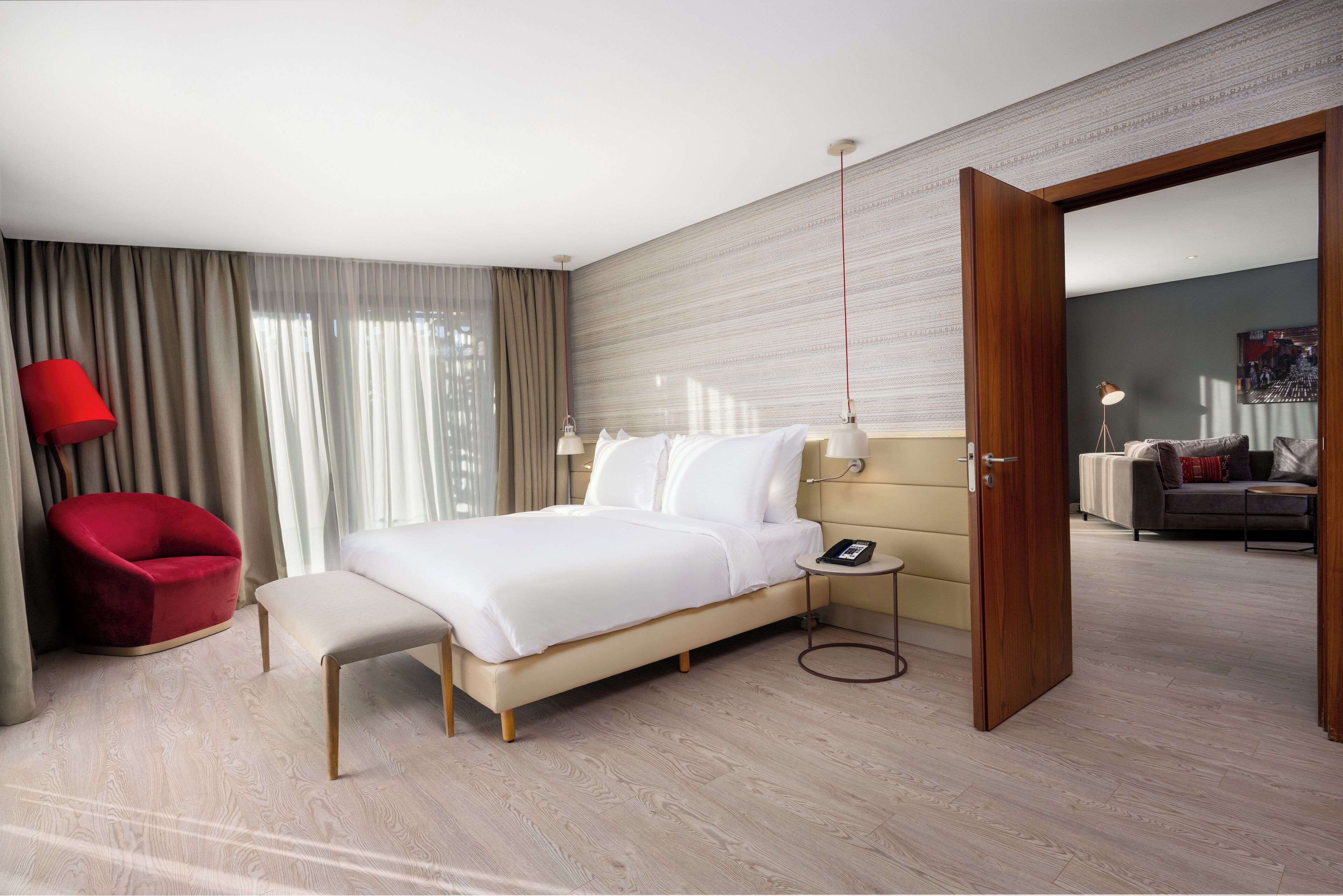 Un hotel moderno con una cama, un sillón rojo, una mesita de noche con lámpara y vistas al área de estar.