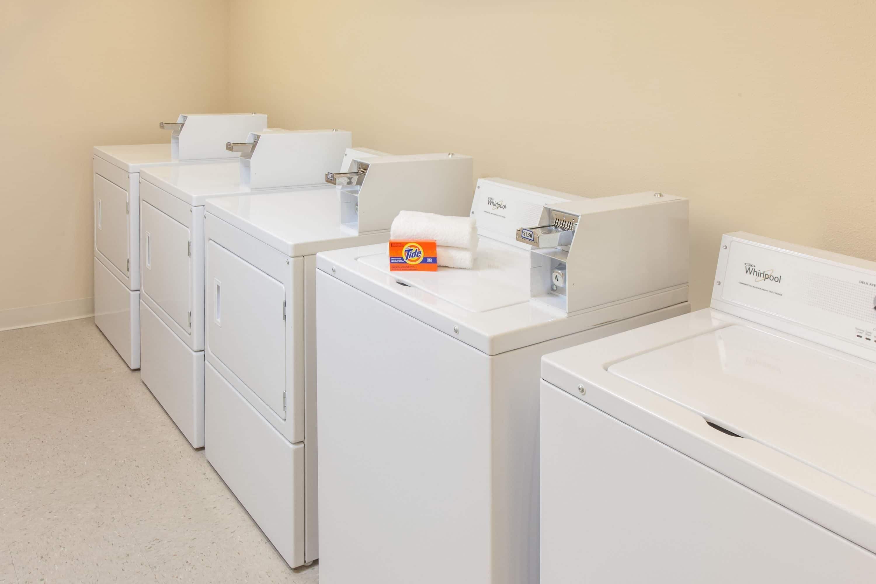 Une buanderie équipée de quatre lave-linge et sèche-linge Whirlpool blancs, d’une boîte de lessive Tide et d’un panneau publicitaire Whirlpool.