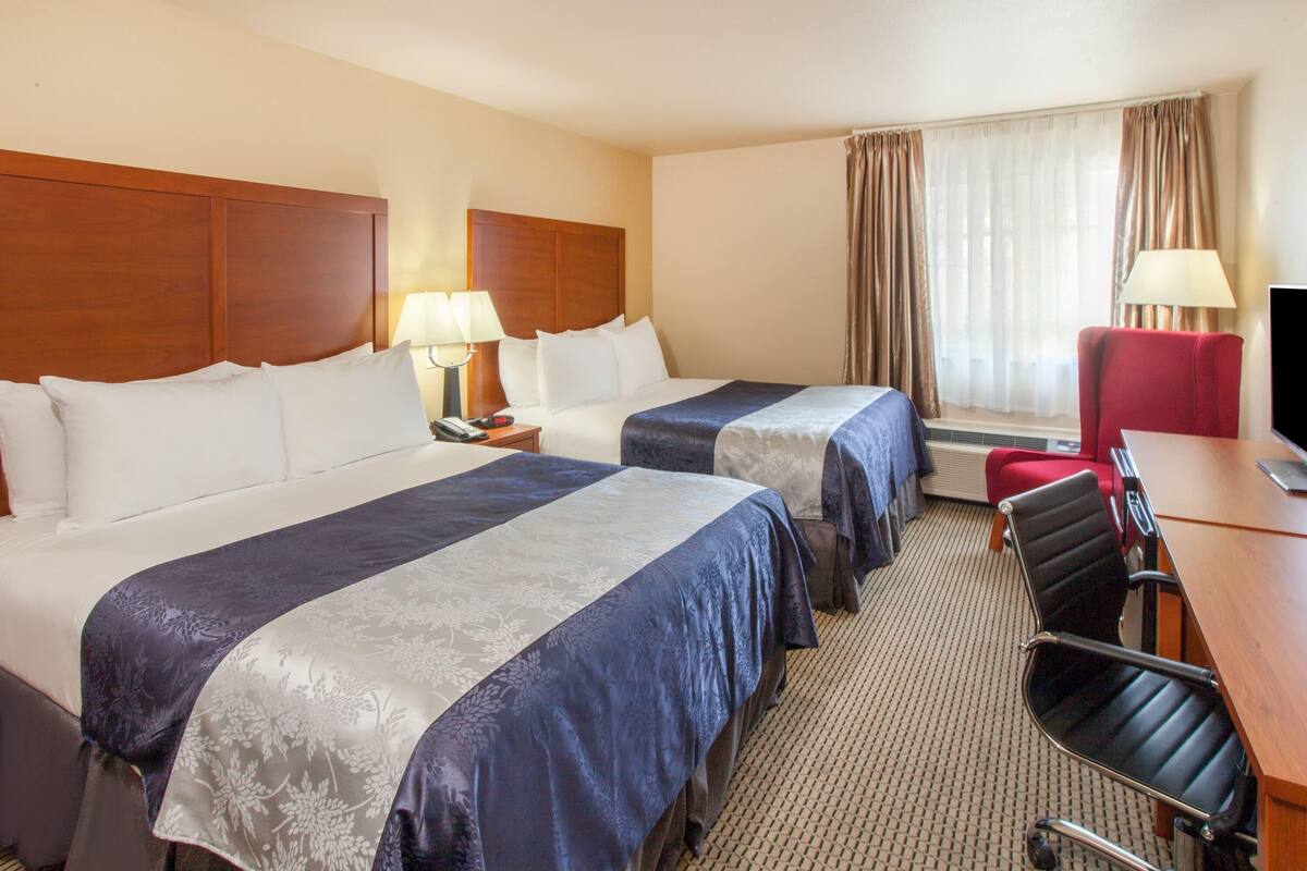 A hotel room with two beds, a desk, a chair, a TV, and a window with curtains.