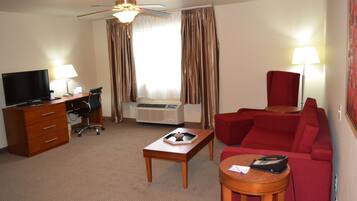 Een hotelkamer met een flatscreen-tv, een bureau met lamp, een rode bank, een klein rond tafeltje en een plafondventilator.