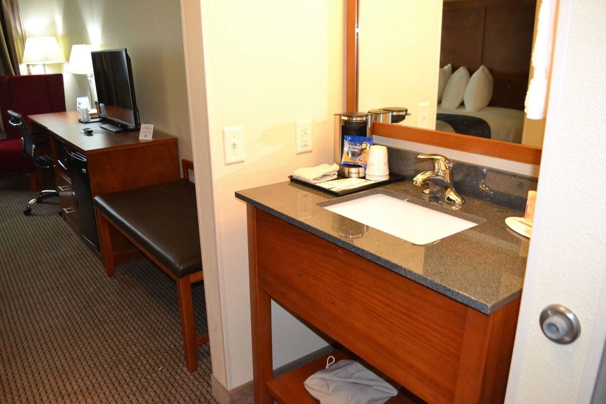 A hotel room with a desk, chair, and a bathroom vanity with a sink and mirror.