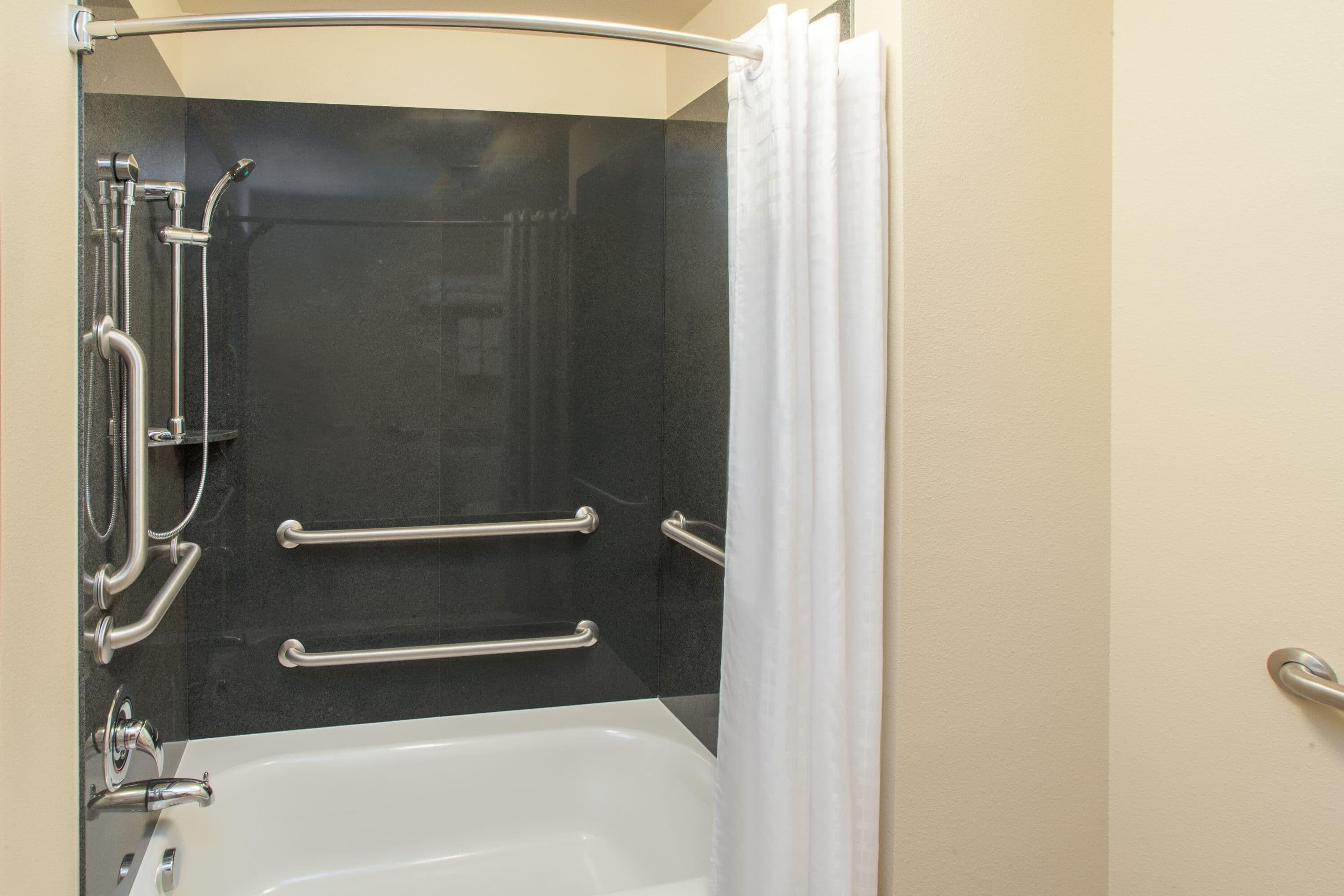 A bathroom with a bathtub, a shower with grab bars, and a curtain.