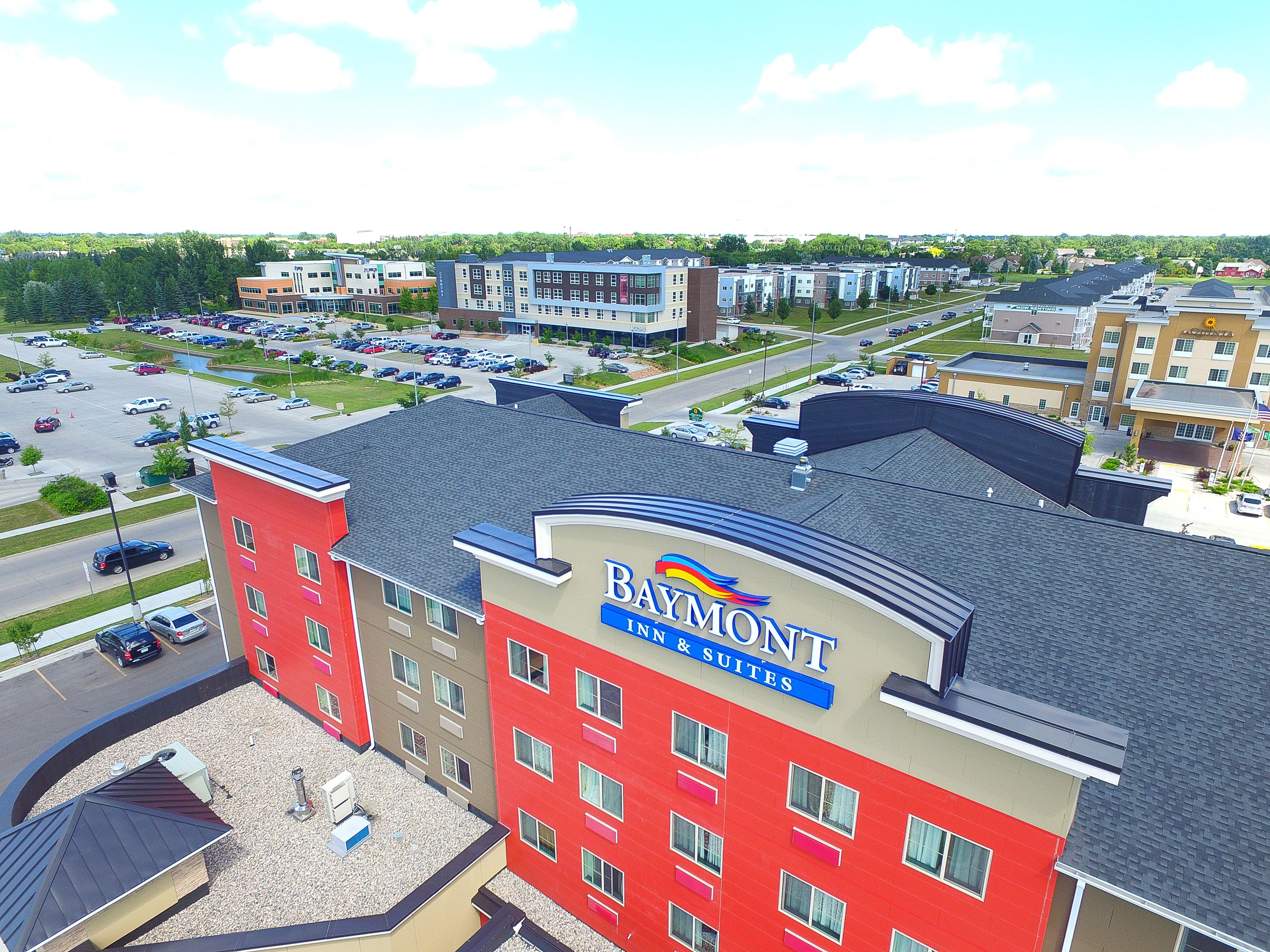 A multi-story hotel with a red and beige facade, a parking lot, and a view of surrounding buildings.