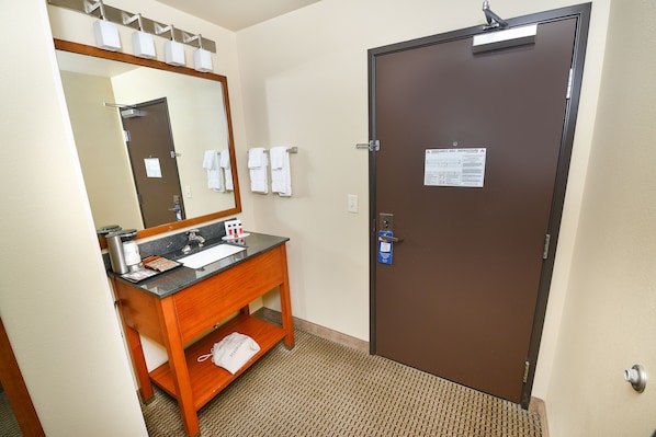 A hotel bathroom with a sink, mirror, towel rack, and a door with a sign.