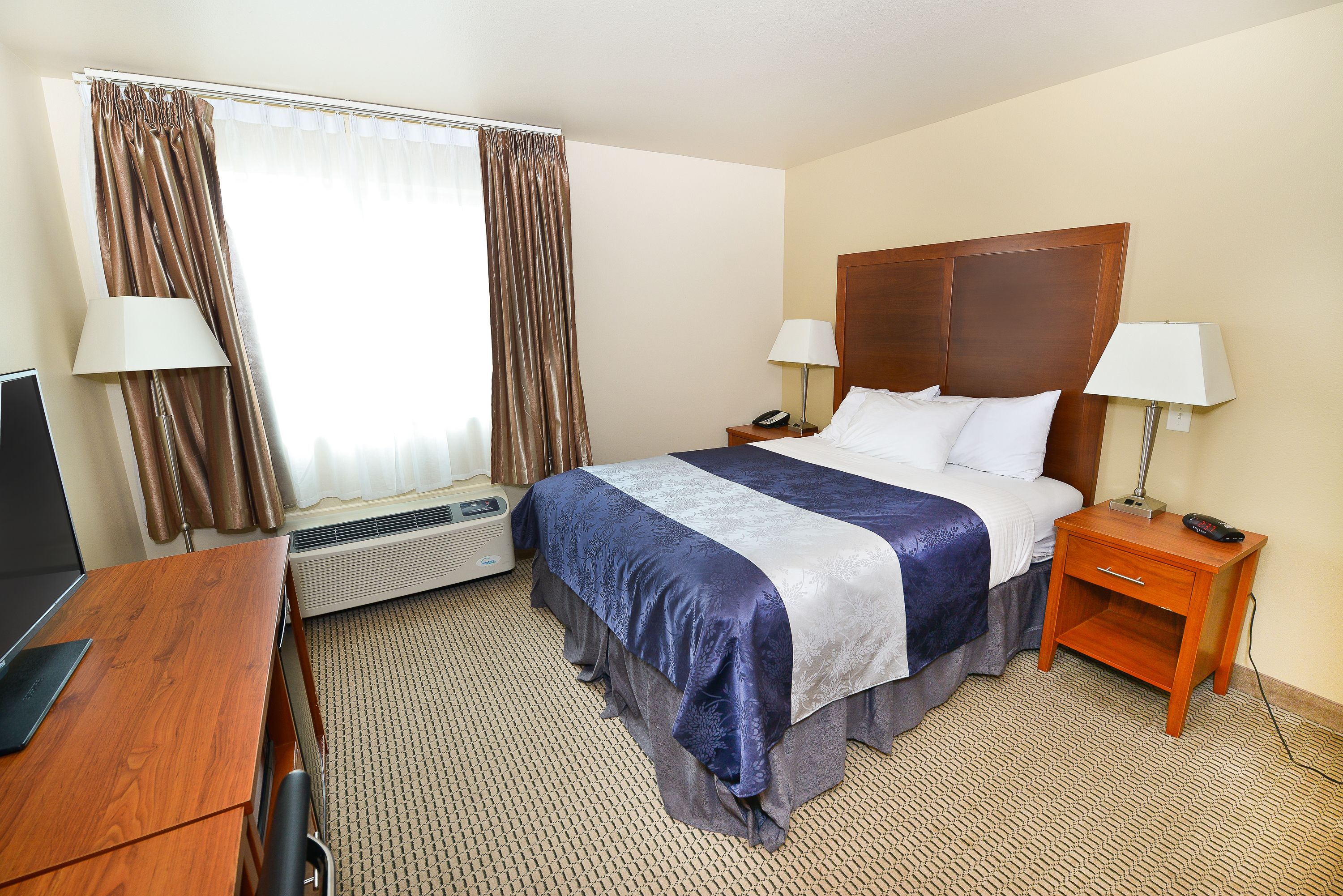 A hotel room with a bed, bedside tables, a desk, and a TV.