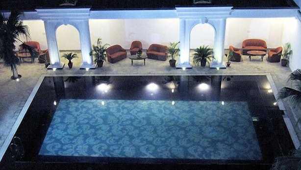 A swimming pool with a patterned floor, surrounded by a covered area with seating and potted plants. - Hotel Ritz Plaza (Amritsar)
