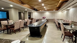 A spacious dining area with a long central table and multiple smaller tables, surrounded by patterned chairs. - Hotel Ritz Plaza (Amritsar)