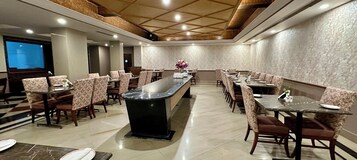 A spacious dining area with a long central table and multiple smaller tables, surrounded by patterned chairs.