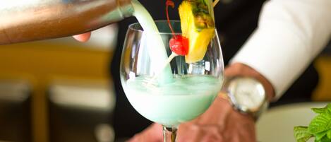 Un bartender sirviendo una bebida en un vaso, con una cereza y una rodaja de piña.