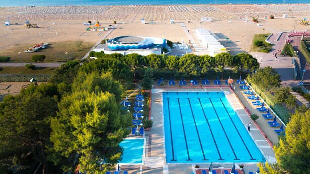 En swimmingpool med tilstødende liggestole og en strand med parasoller og solstole.