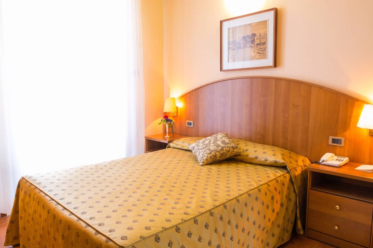 Ein Hotelzimmer mit einem großen Bett, einem Holzkopfbrett, Nachttischlampen, einem Telefon und einem gerahmten Bild an der Wand.