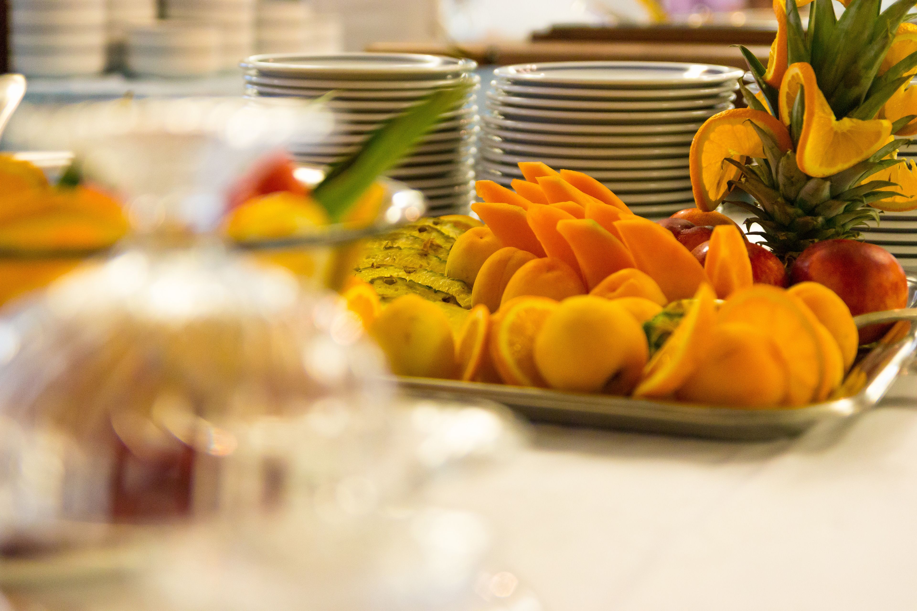 A buffet table with various fruits and stacked plates.