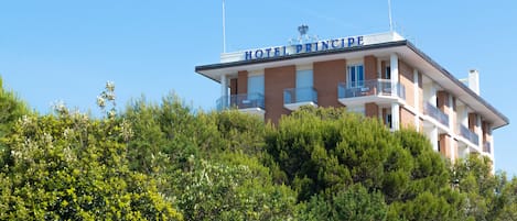 Un hotel llamado "Hotel Principe" con un balcón en la planta superior, rodeado de abundante vegetación.
