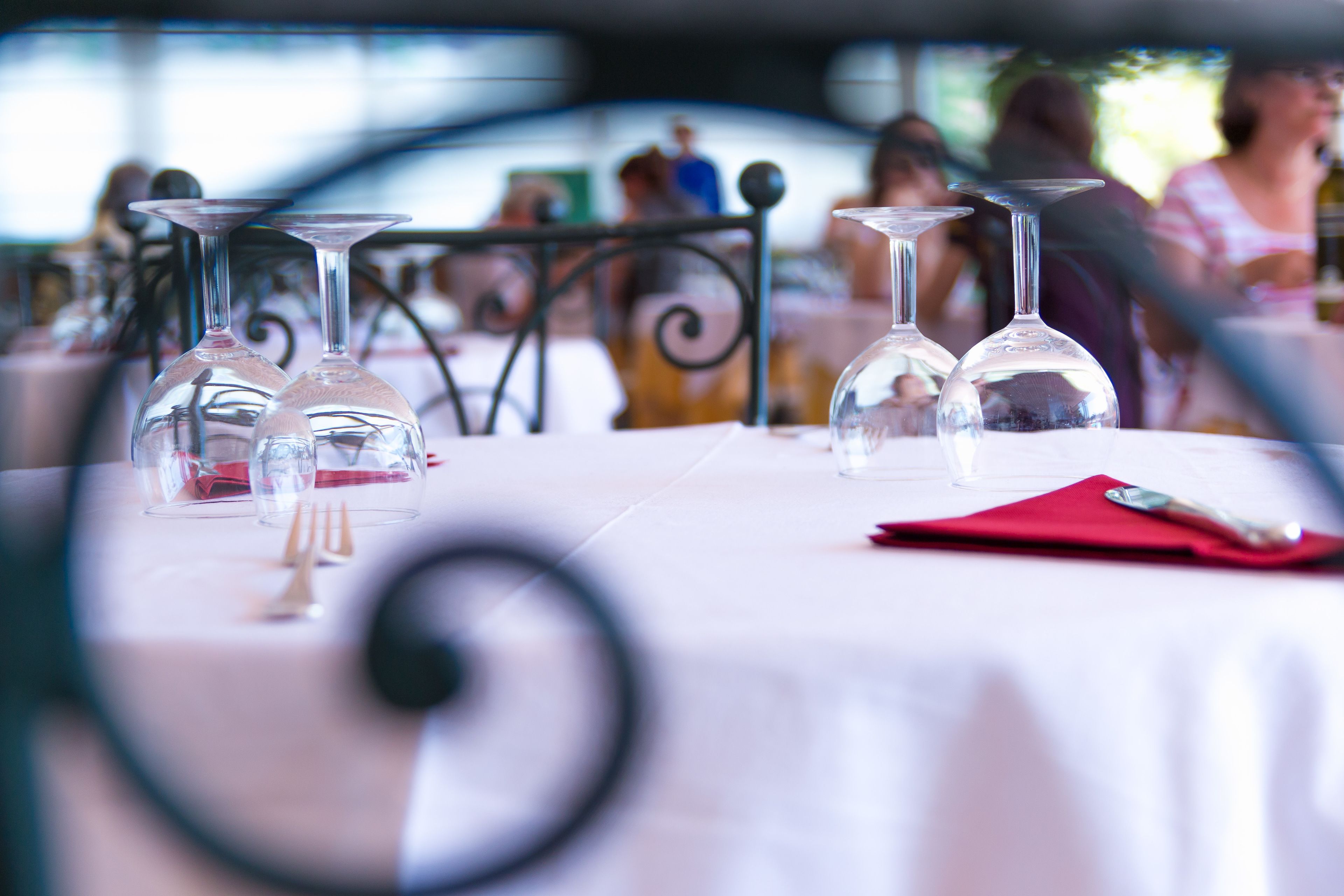 Mesa lista para una comida, con copas de vino, un tenedor y un mantel individual rojo.