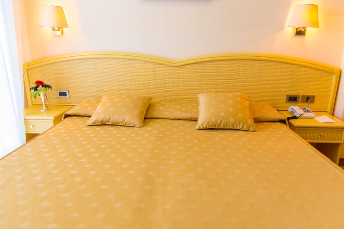 Ein Hotelzimmer mit einem großen Bett, zwei Nachttischlampen, einem Nachttisch mit Telefon und Lampe sowie einer Vase mit Blumen.
