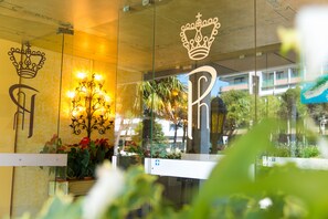 Un hall d’accueil d’hôtel avec un logo en forme de couronne, un lustre et une plante en pot.