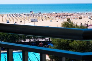 Une plage bordée de rangées de transats et de parasols, une piscine et une vue sur la mer.