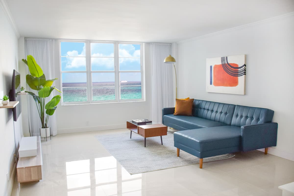 A modern living room with a blue sofa, a coffee table, and a large window with a view of the ocean.