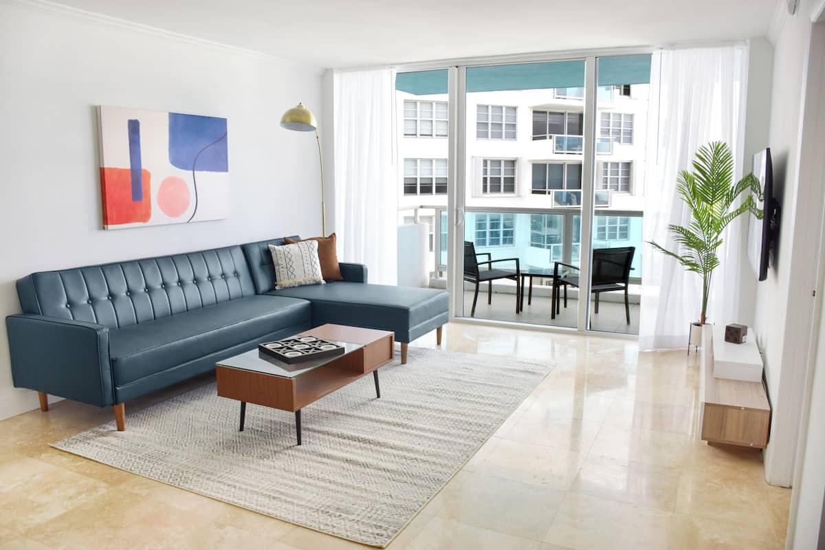 A modern living room with a sectional sofa, a coffee table, and a large sliding glass door leading to an outdoor balcony.