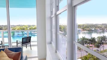 A spacious room with large windows offering views of a body of water and a bridge. There is a blue sofa with cushions and a chair.