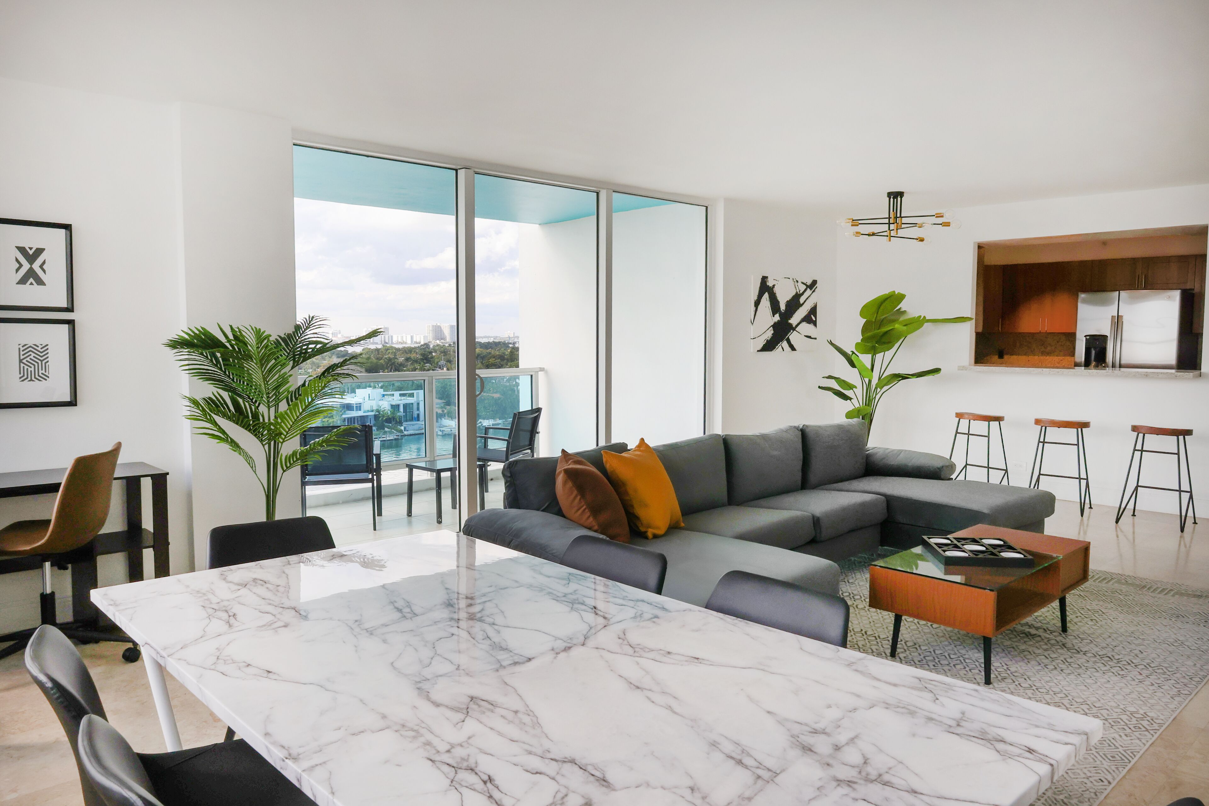 Una sala de estar moderna con un amplio ventanal corredera, un sofá seccional gris, una mesa de centro de mármol y una cocina de diseño minimalista.