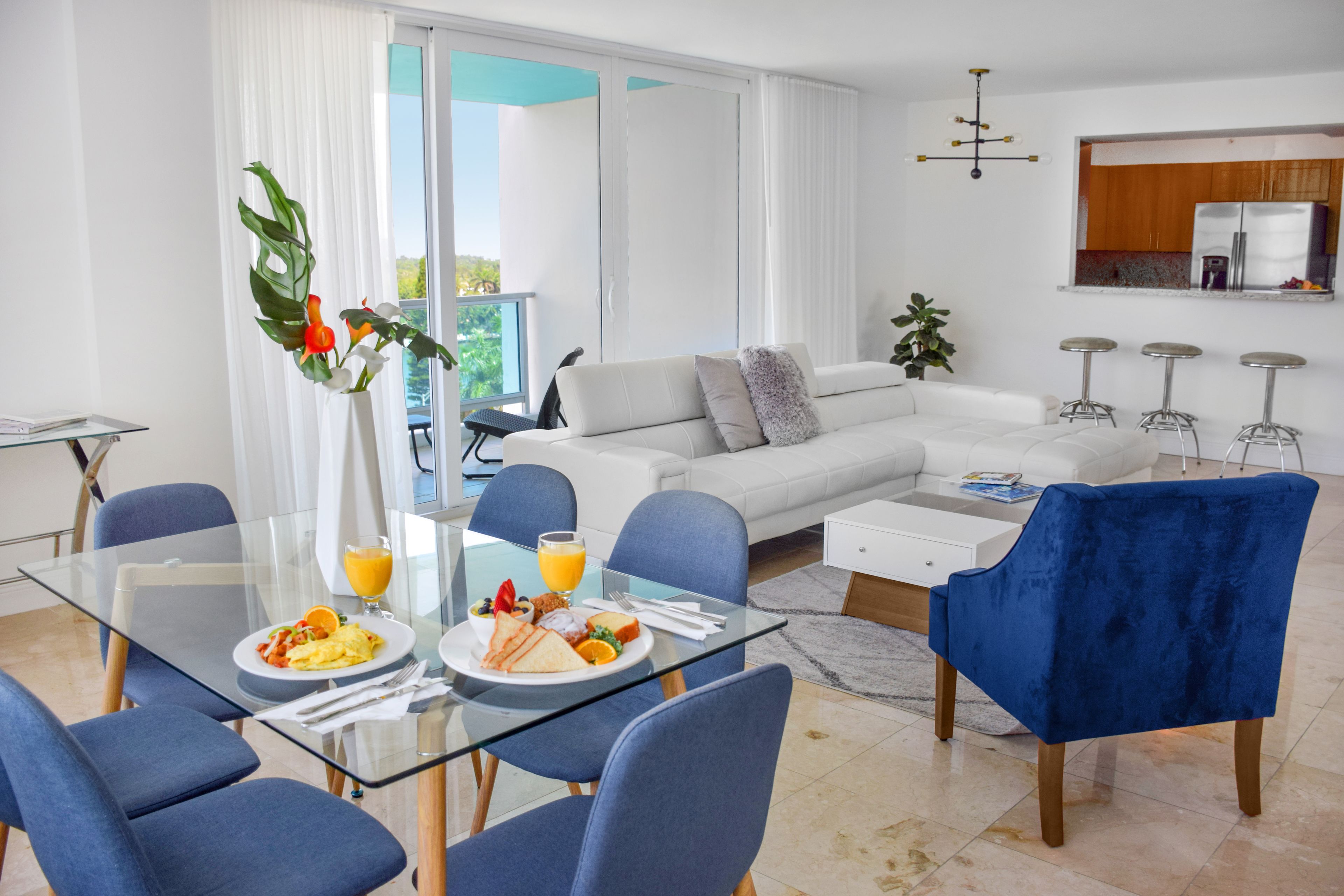 Ein modernes Wohnzimmer mit einem Glastisch, blauen Stühlen, einem weißen Sofa und einem blauen Samt-Sessel.
