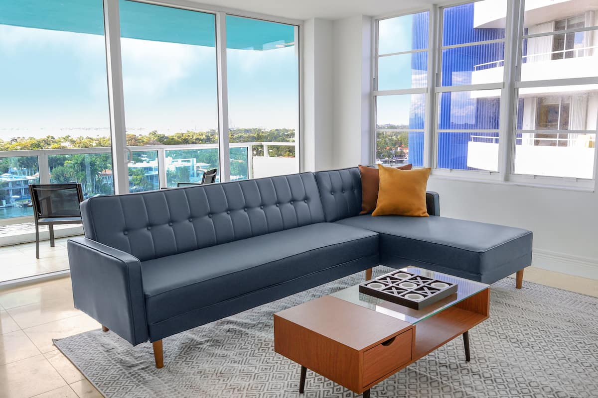A modern living room with a dark blue sectional sofa, a glass coffee table, and a patterned rug.