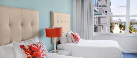 A hotel room with two beds, a red lamp, and a view of a cityscape through large windows.