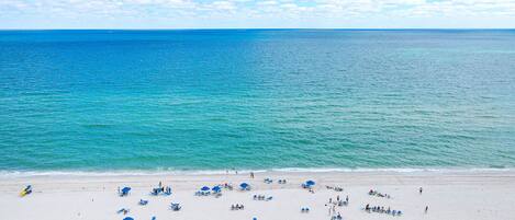 A beach with white sand, clear blue water, and a few people.