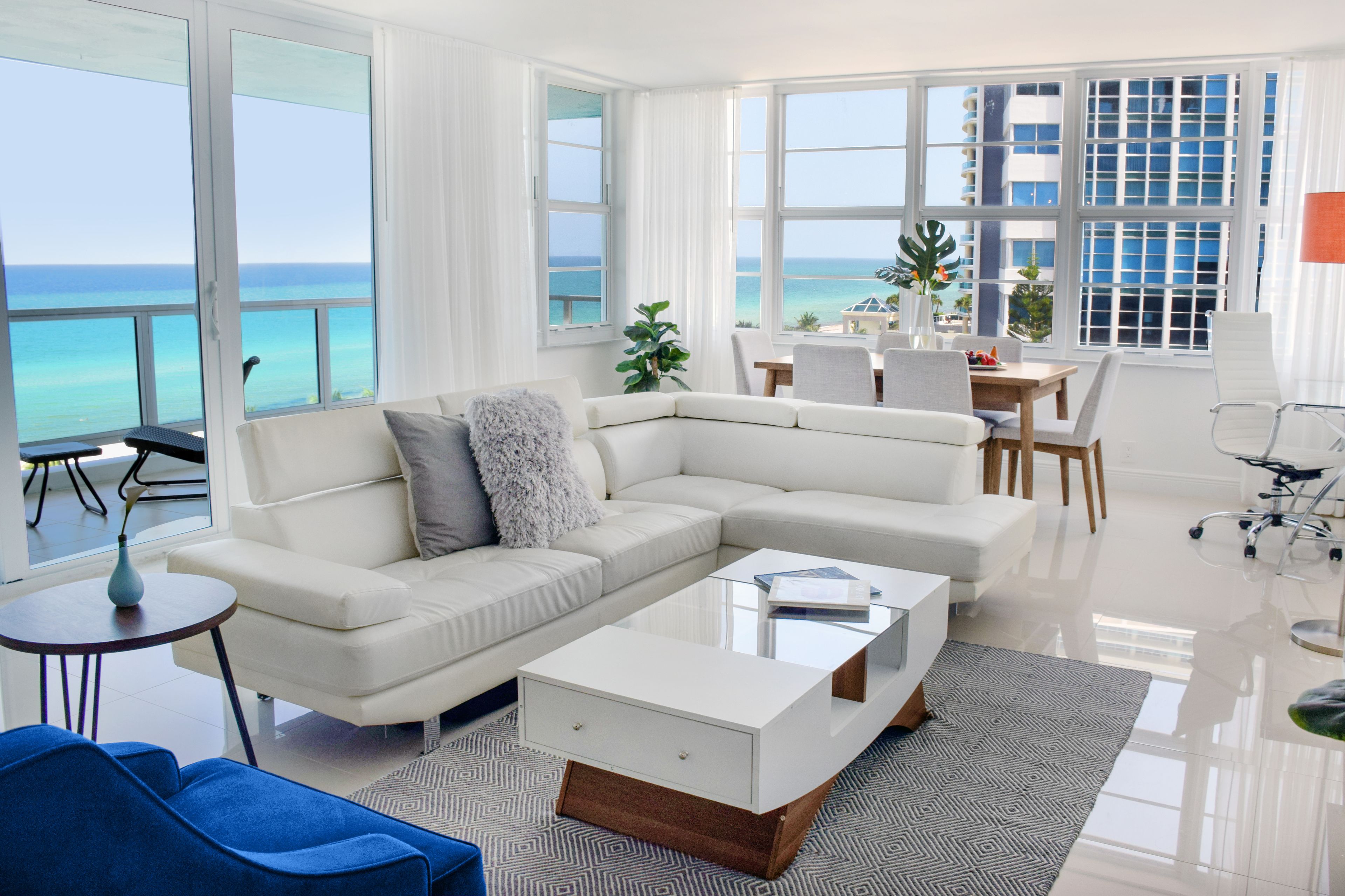 A modern living room with a white sectional sofa, a glass coffee table, and a view of the ocean.
