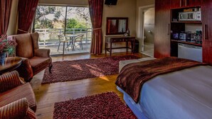 A hotel room with a bed, two chairs, a small table, a TV, and a kitchen area with a microwave. - A&A Guesthouse (Gqeberha (Port Elizabeth))
