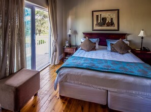 A hotel room with a large bed, a bench, a nightstand, a lamp, and a painting on the wall. - A&A Guesthouse (Gqeberha (Port Elizabeth))
