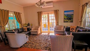 A living room with a patterned rug, leather sofas, and a painting on the wall. - A&A Guesthouse (Gqeberha (Port Elizabeth))