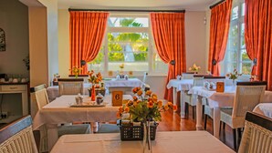 A dining area with tables set for service, numbered place cards, and a view of the outdoors through large windows. - A&A Guesthouse (Gqeberha (Port Elizabeth))